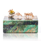 A rectangular jewelry box made of green malachite with gold-toned animal figures on top, including a crab and an elephant, photographed on a white reflective surface.